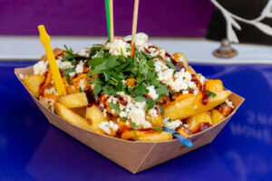 Fried potatoes fries grated cheese on top, parsley during fast food festival. Outside catering.
